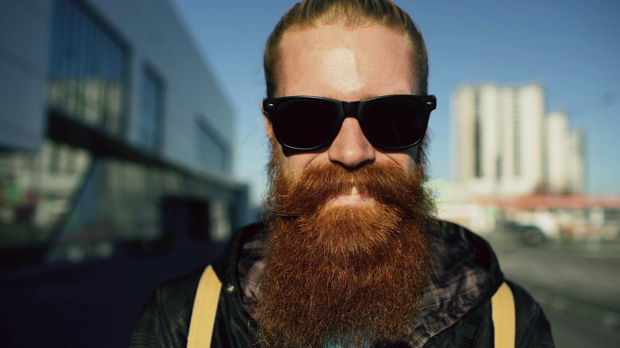 Closeup portrait of young bearded hipster man in sunglasses smiling and posing while travelling at city street