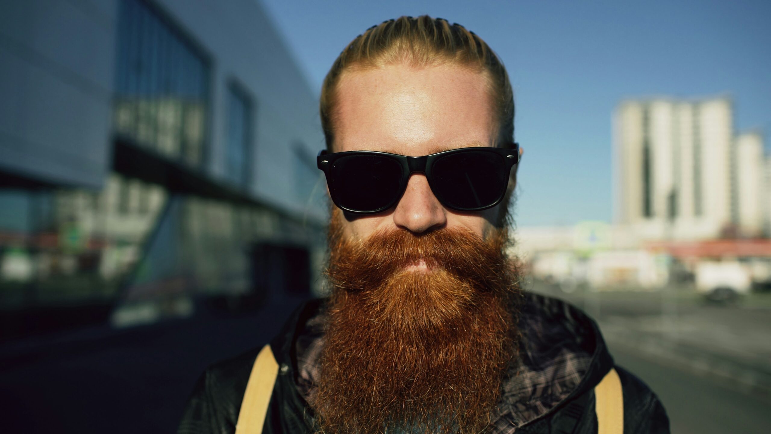 Closeup portrait of young bearded hipster man in sunglasses smiling and posing while travelling at city street